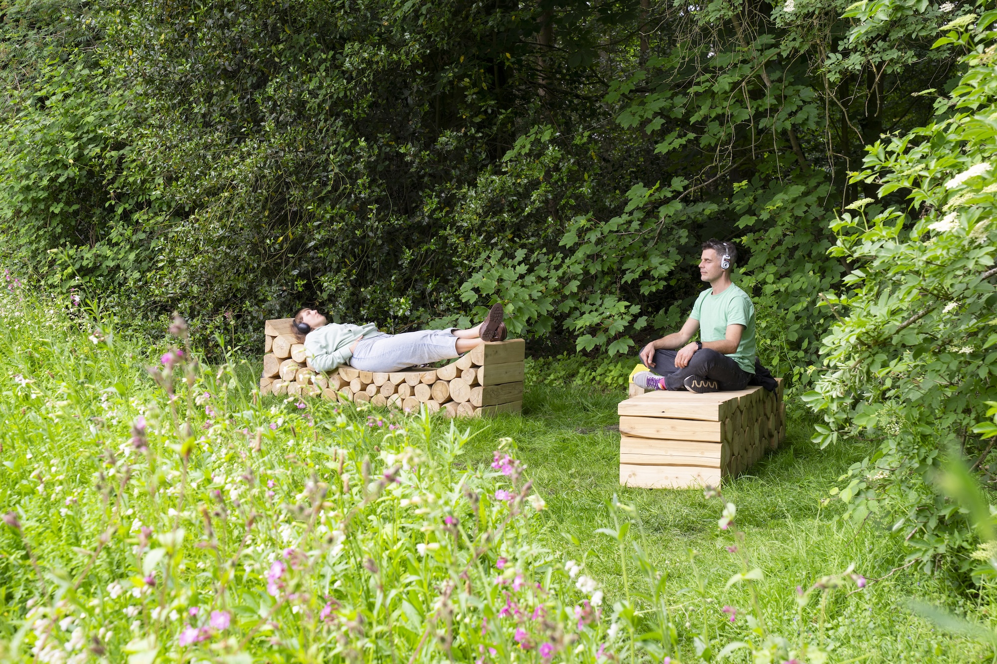 Zwei Menschen mit Kopfhörern entspannen sich auf Holzbänken