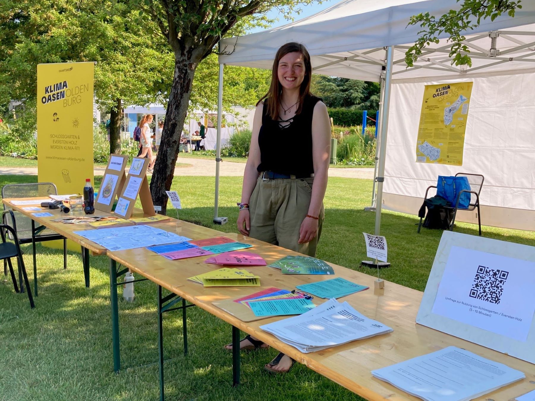 Lea Vilchez steht hinter einem bunt mit Flyern bestückten Infostand im Park