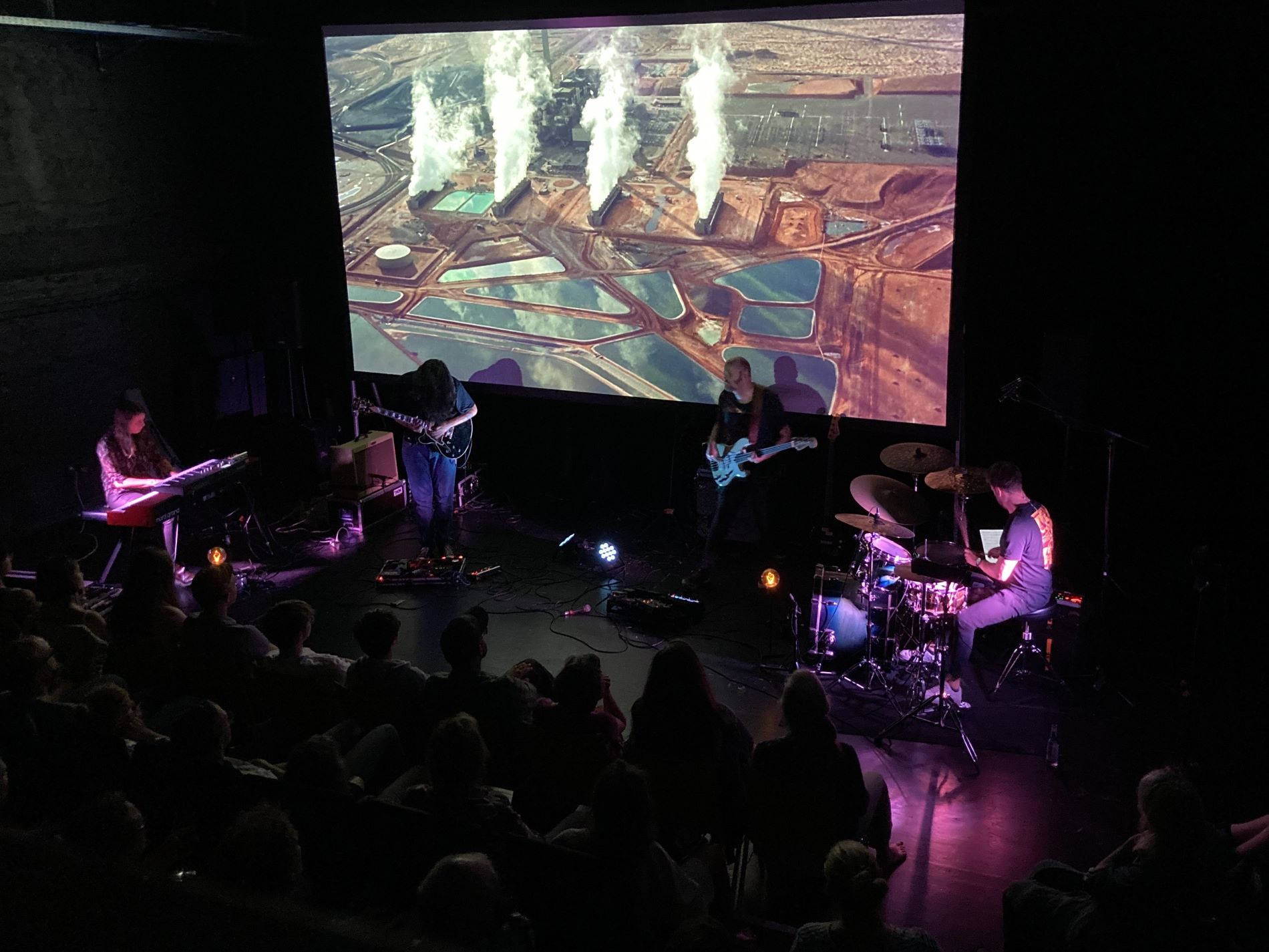 Filmleitwand zeigt den Film "Koyaanisqatsi", Band im Vordergrund.